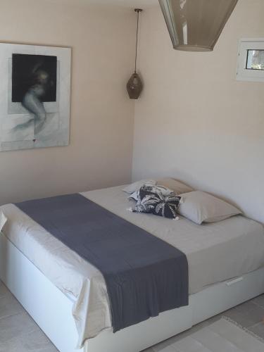 - un lit dans une chambre blanche avec une photo sur le mur dans l'établissement Les Bromélias Ile du Levant, à Hyères