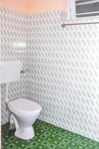 a bathroom with a white toilet and a green floor at Palm Resort in Gūdalūr