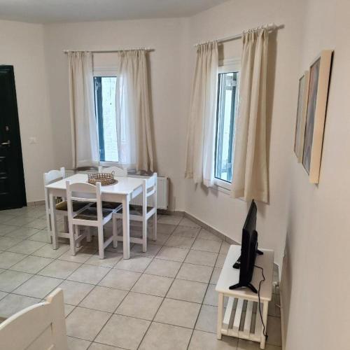 a white dining room with a table and a tv at Andros Eco Home in Gavrion