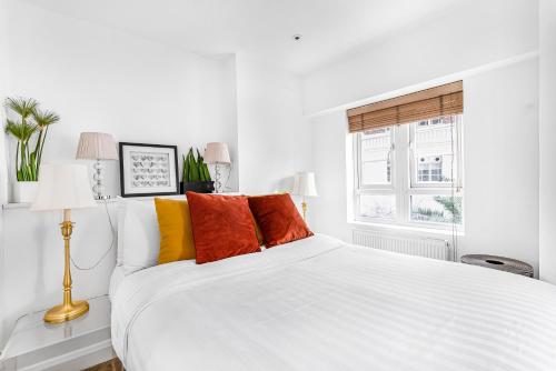 a white bed with colorful pillows in a white bedroom at Elegant 1 Bedroom flat near Harrods in London