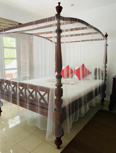 a wooden canopy bed with white sheets and red pillows at Sagarika Beach Hotel in Moragalla