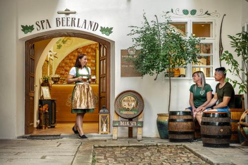 Una donna in piedi davanti a un negozio con due persone di Spa Beerland - At The Golden Lamb a Plzeň