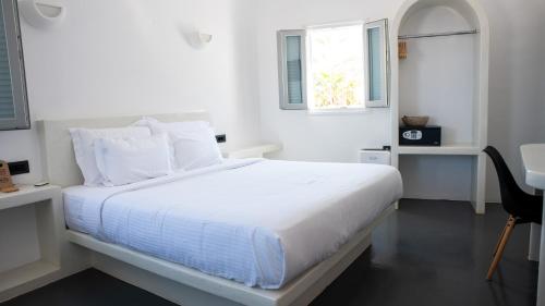 a white bedroom with a white bed and a window at White Cave Villas in Oia