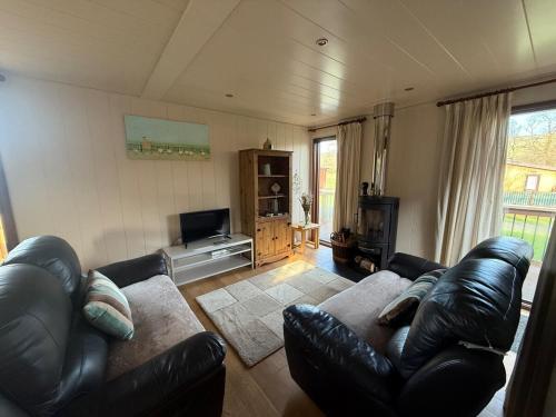 a living room with a leather couch and a television at Charming 2 bedroom Cabin In the Shropshire Countryside with Fantastic Views in Clunton