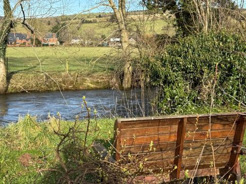 a wooden bench sitting next to a river at Charming 2 bedroom Cabin In the Shropshire Countryside with Fantastic Views in Clunton