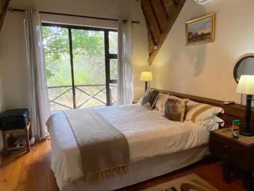 ein Schlafzimmer mit einem Bett und einem großen Fenster in der Unterkunft Buster's River Lodge in Marloth Park