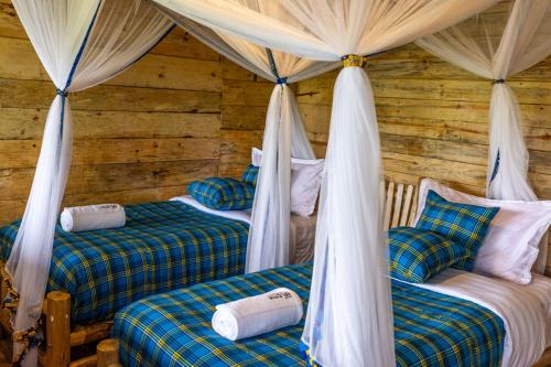 two beds in a log cabin with drapes at Nyanja View Resort in Fort Portal