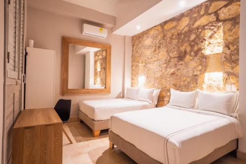 una camera d'albergo con due letti e una parete in pietra di Casa Catalina De Mokana By SoHo a Cartagena de Indias