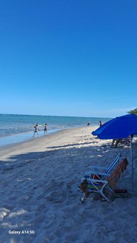 a beach with a chair and an umbrella and people on the beach at Suite privativa santinho in Porto Seguro