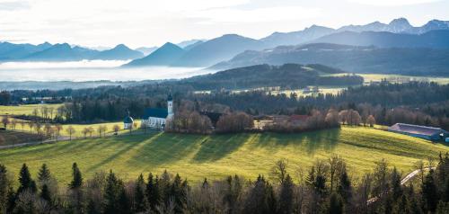 a farm in a field with mountains in the background at Hotel Irschenberg Süd in Irschenberg