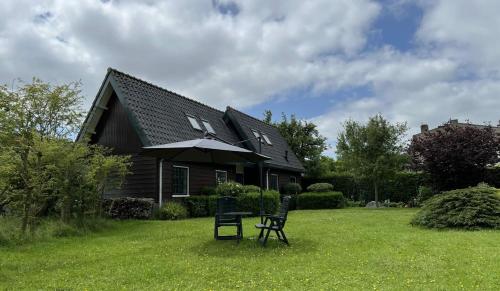a house with two chairs and an umbrella in the yard at Bed & Breakfast Kortenhoefsedijk in Kortenhoef