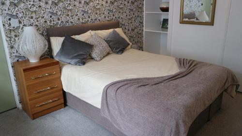 a bed with pillows and a night stand with a lamp at Peterborough House in Saint Aubin