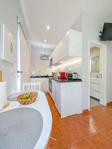 a kitchen with white cabinets and a table with a bowl of fruit at Casas das Hortas, Studio Vista Jardim e Serra in Seixal