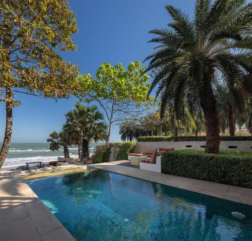 a swimming pool next to a beach with palm trees at Villa Maroc Resort in Pran Buri