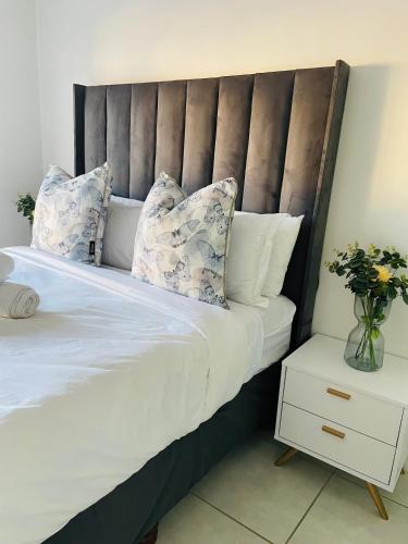 a bed with white sheets and pillows and a vase of flowers at 2 Bedroom- The Blyde by Given in Pretoria