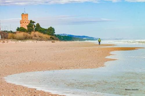 a person walking on a beach with a lighthouse in the distance at Appartamenti turistici di Gabriele 20 mt dal mare in Pineto