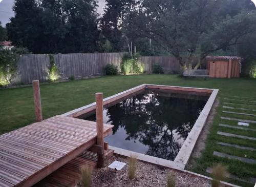 un étang dans un jardin avec une terrasse en bois dans l'établissement Villa du Bois des Écureuils, à Saint-Laurent-de-la-Prée