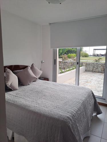 a white bedroom with a bed and a large window at Apart Altos del Virrey in Colonia del Sacramento