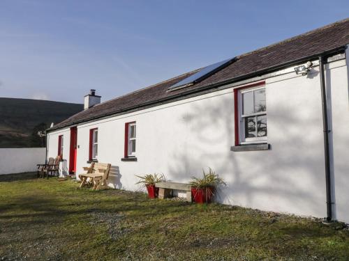 a white building with red windows and a table and benches at Dan White's Cottage in Newry