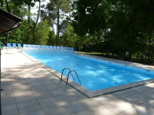 une grande piscine bleue avec des chaises et des arbres dans l'établissement Villa Mimosa Comfortable holiday residence, à Lacanau
