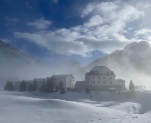 a building in the snow in front of a mountain at Hotel Maloja Kulm in Maloja