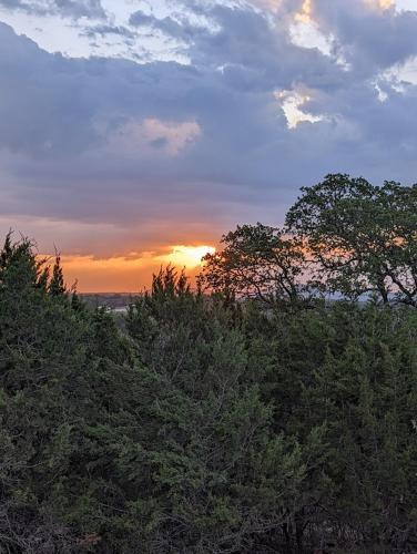 a sunset over trees with the sun setting in the background at Boulderdash Birdhouse Studio in Bandera