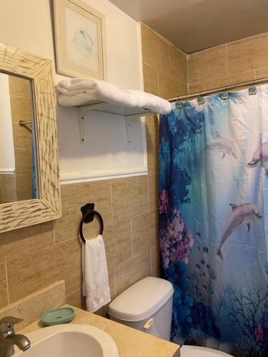a bathroom with a toilet and a shower curtain with dolphins at Bayahibe Cadaques Caribe Apartment in Bayahibe