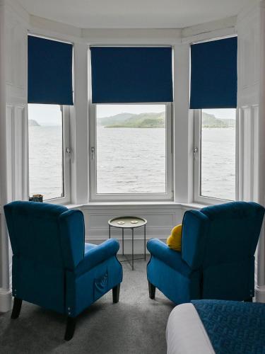 two blue chairs and a table in a room with windows at MacKays in Oban