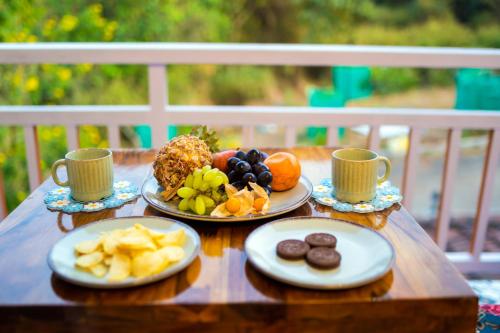 a wooden table with plates of fruit and cups on it at La Mira Casa Karjat in Karjat