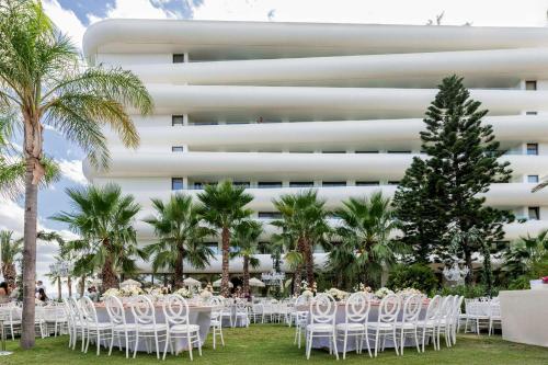 a table with white chairs in front of a building at Isla Brown Corinthia Resort & Spa, Curio Collection by Hilton in Agioi Theodoroi