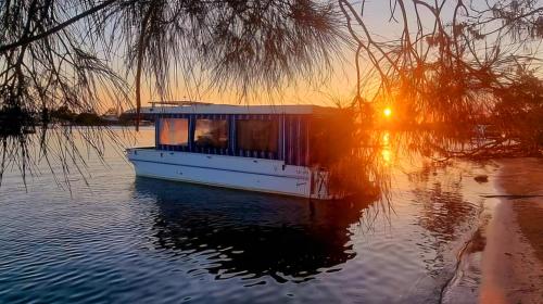 a small boat in the water at sunset at Liquid PARIDISE Noosaville houseboat "Experience More" in Noosa Heads