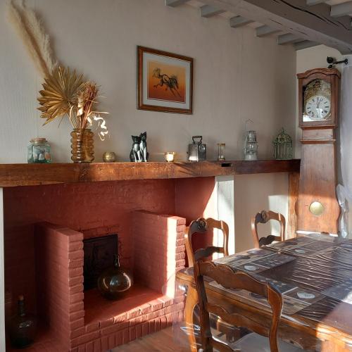 - un salon avec une cheminée en briques, une table et une horloge dans l'établissement La ferme des aristochats, à Blicourt