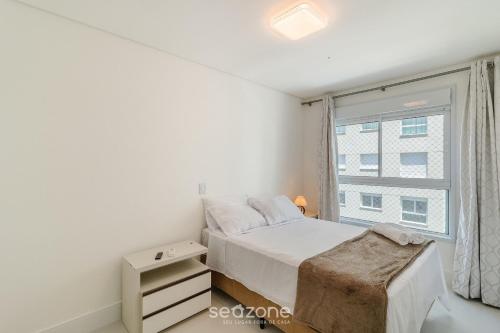 a white bedroom with a bed and a window at Condomínio a beira-mar c/ piscina - SHC in Piçarras