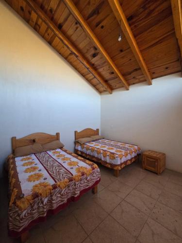 two beds in a room with a wooden ceiling at Cabaña el Pino in Penche Chico