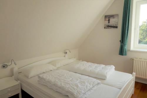 Una cama blanca en una habitación con ventana. en Ferienhaus Sturmfrei auf Fehmarn, en Kopendorf