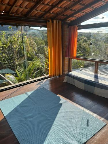 Habitación con ventana grande y alfombra azul. en Casa Águia Dourada Vale do Capão, en Caeté-Açu