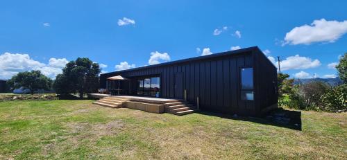 a black house sitting on top of a grass field at Coastal Haven, Ahipara Escape in Ahipara
