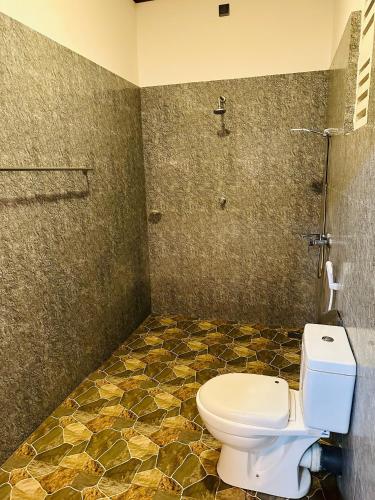 a bathroom with a toilet and a tiled floor at Ceylon Safari Cottage in Udawalawe