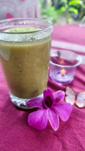 a glass of juice and a purple flower on a table at Mallis Guesthouse in Habaraduwa