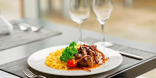 a plate of pasta with meat and vegetables and two wine glasses at PLAZA Residence Stuttgart-Ditzingen in Ditzingen