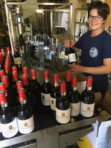 Une femme debout à côté d'une bande de bouteilles de vin dans l'établissement Château Doyac, à Saint-Seurin-de-Cadourne