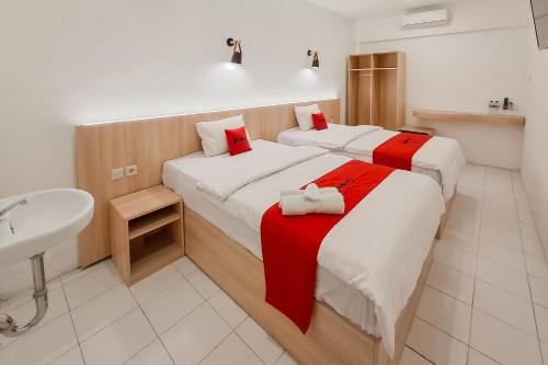 two beds in a room with a sink and a bathroom at RedDoorz at Grand Mirza Near Pasar Grosir Batik Setono Pekalongan in Pekalongan