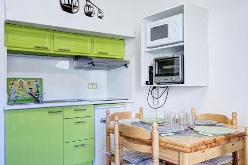 une cuisine avec des placards verts, une table et un four micro-ondes dans l'établissement Le Petit Montagnard - Station accessible à pied, aux Angles