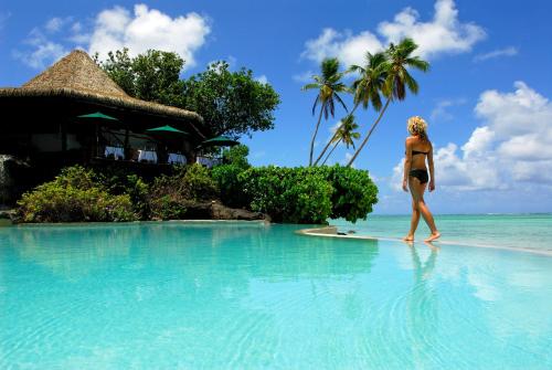 a woman walking on a surfboard in the water at a resort at Pacific Resort Aitutaki - Adults Only in Arutanga