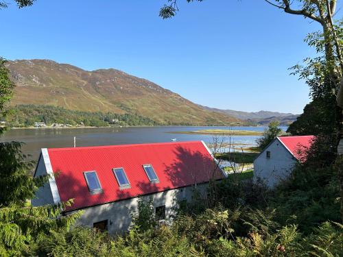 a house with a red roof next to a lake at An Iolaire in Dornie