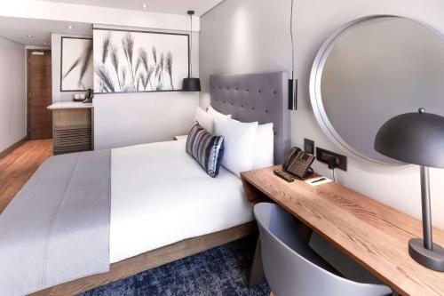 a bedroom with a bed and a desk and a mirror at SunSquare Cape Town City Bowl in Cape Town