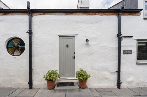 a white building with a door and two potted plants at Tan Y Fron By Birch Stays in Pentraeth