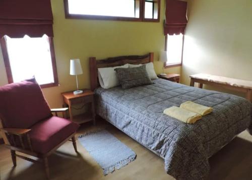 a bedroom with a bed and a chair and windows at ECOHOSTAL HUELLAS DEL BOSQUE in Valdivia