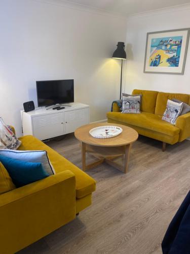 a living room with two yellow couches and a coffee table at Avocet Cottage Sheringham in Sheringham