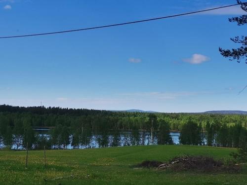 a green field with a lake in the background at Humlehjarta family room, 3 separate beds in Överkalix